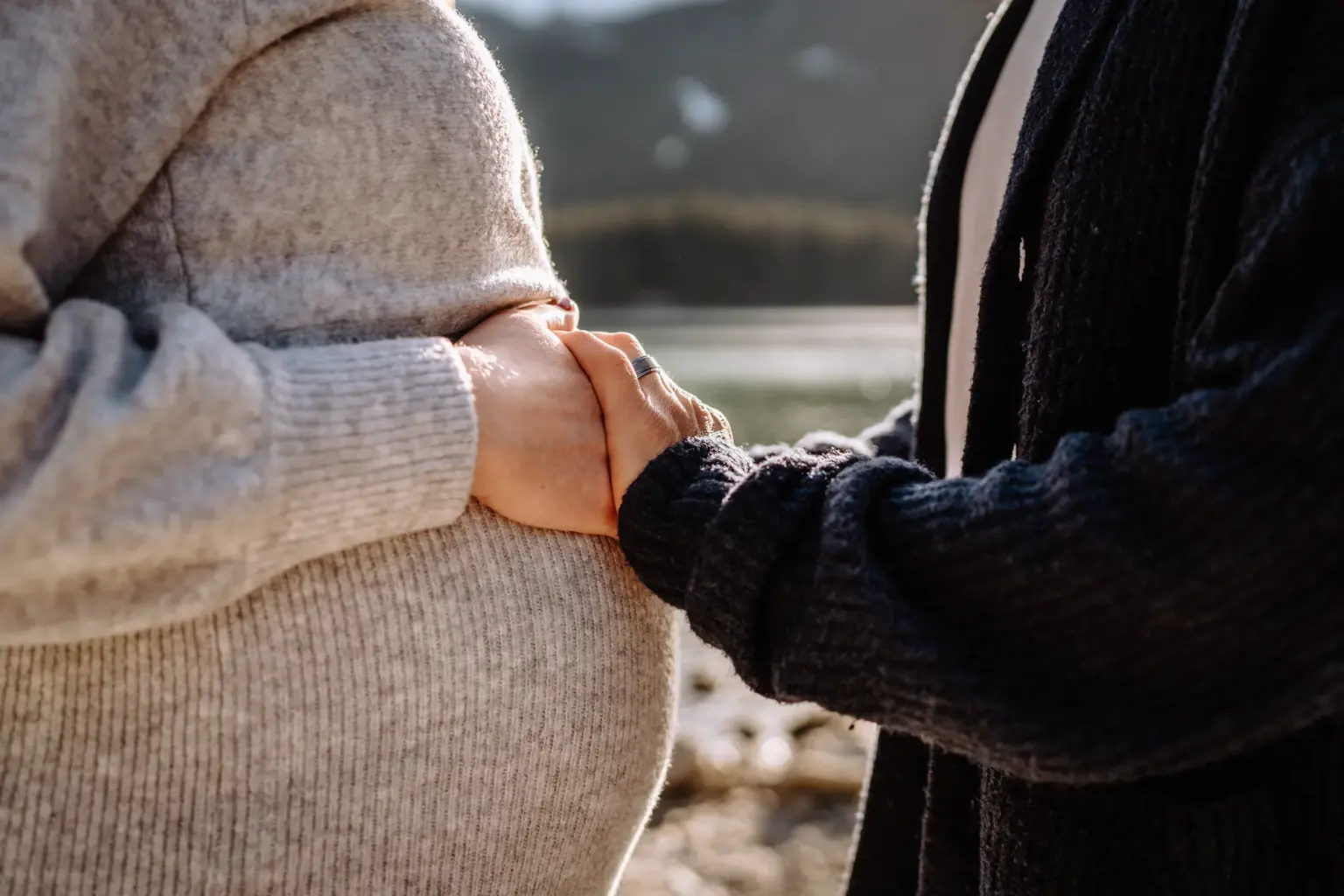 Paar hält gemeinsam den Babybauch mit dem Eibsee im Hintergrund