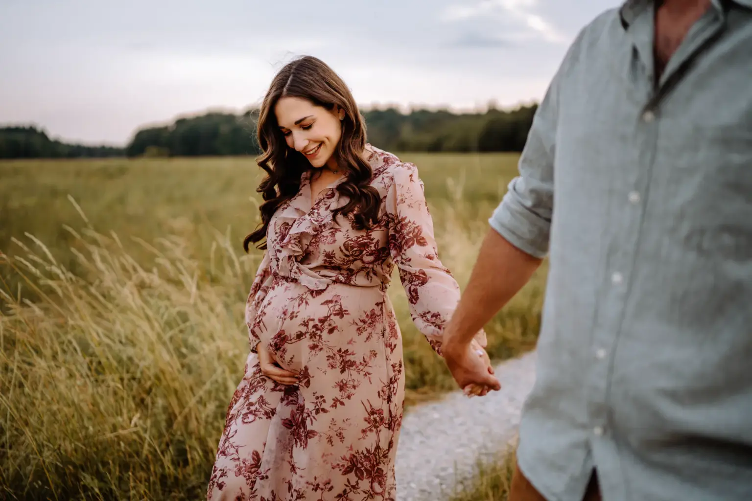 Hände halten sich, Babybauch im Vordergrund, beide laufen glücklich Hand in Hand