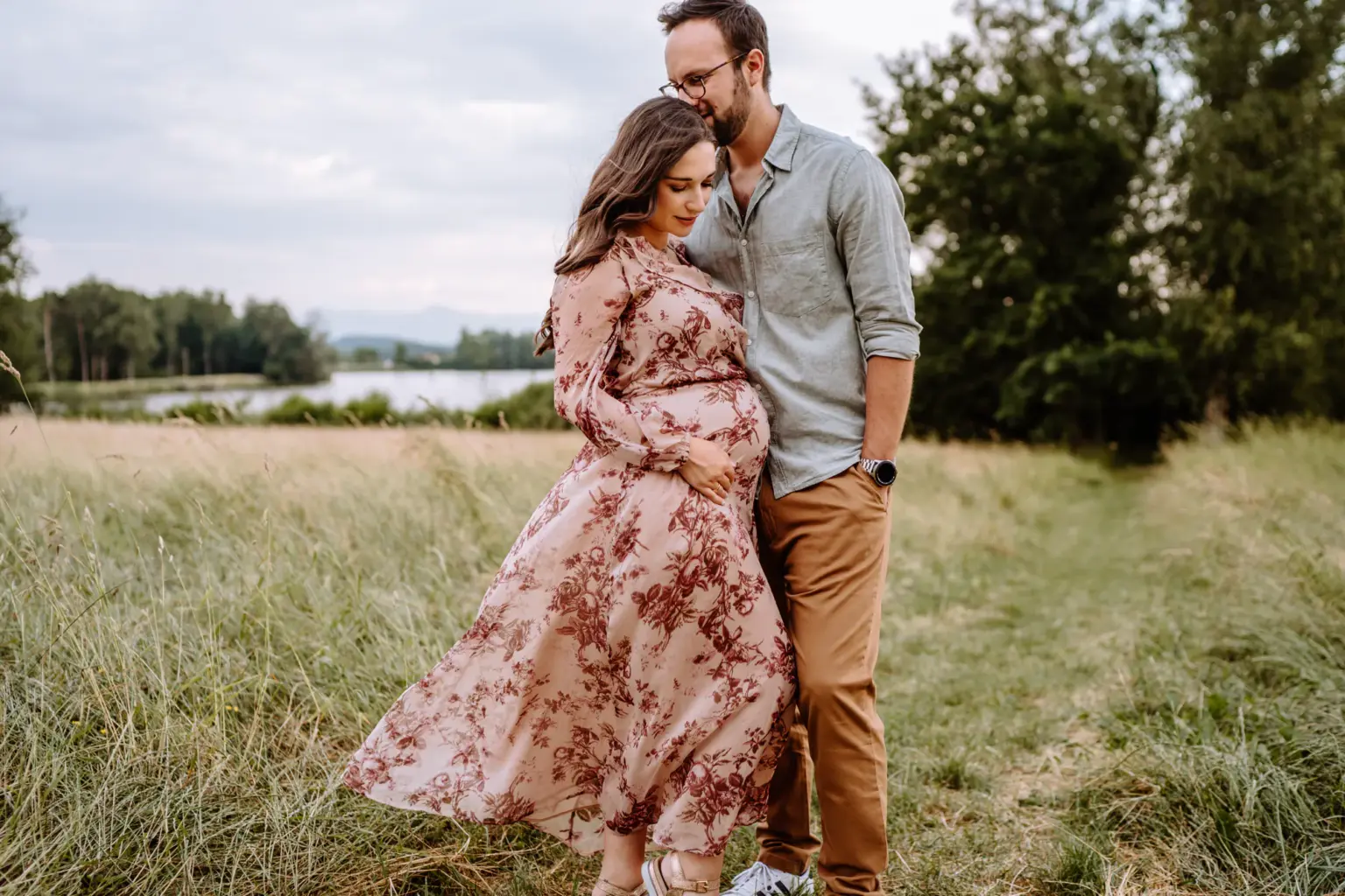 Paarfoto mit Babybauch am Seeufer, beide schauen aufs Wasser, innige Stimmung