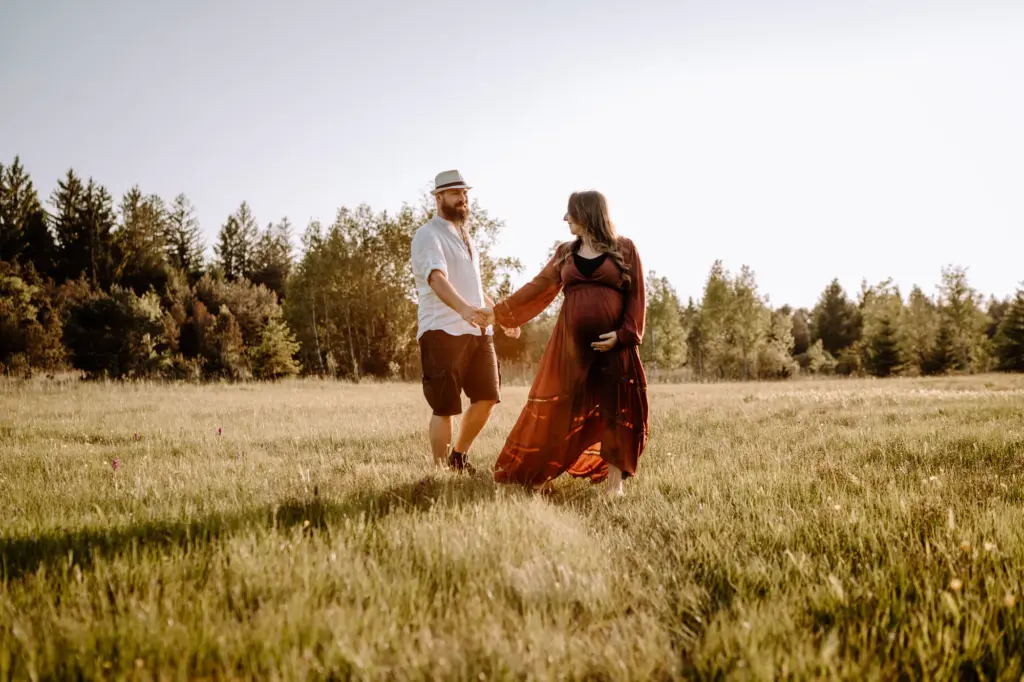 Schwangere im Leihkleid auf der Wiese, fließender Stoff im Abendwind