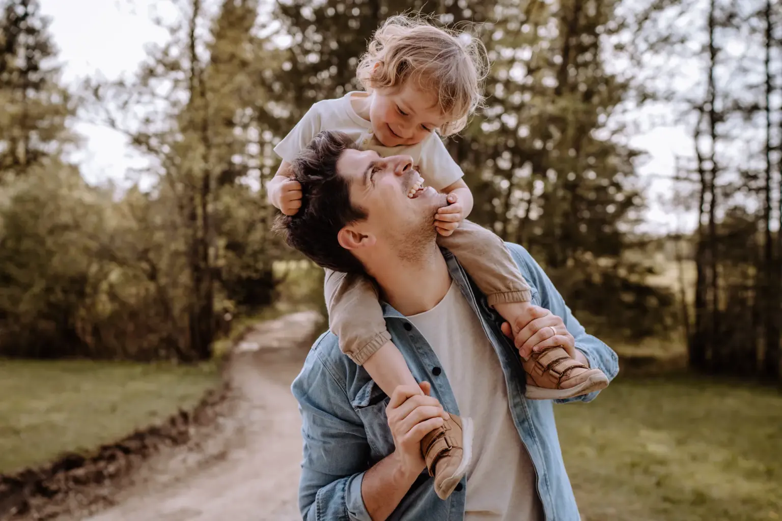 Papa trägt sein Kind auf den Schultern und beide schauen sich in die Augen