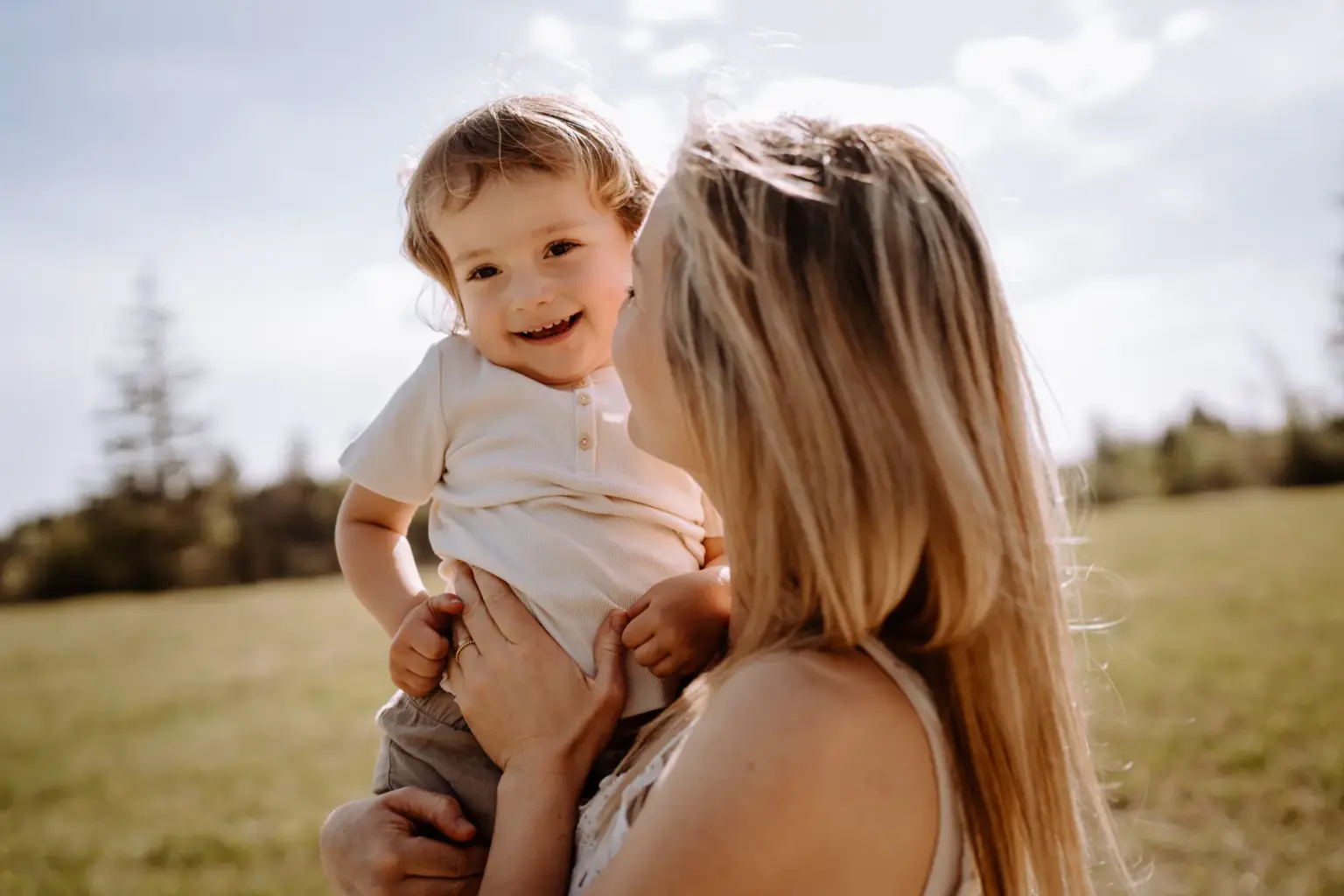 Mama trägt ihr Kind auf dem Arm und das lächelt in die Kamera bei angestellten Familienfotos in der Natur