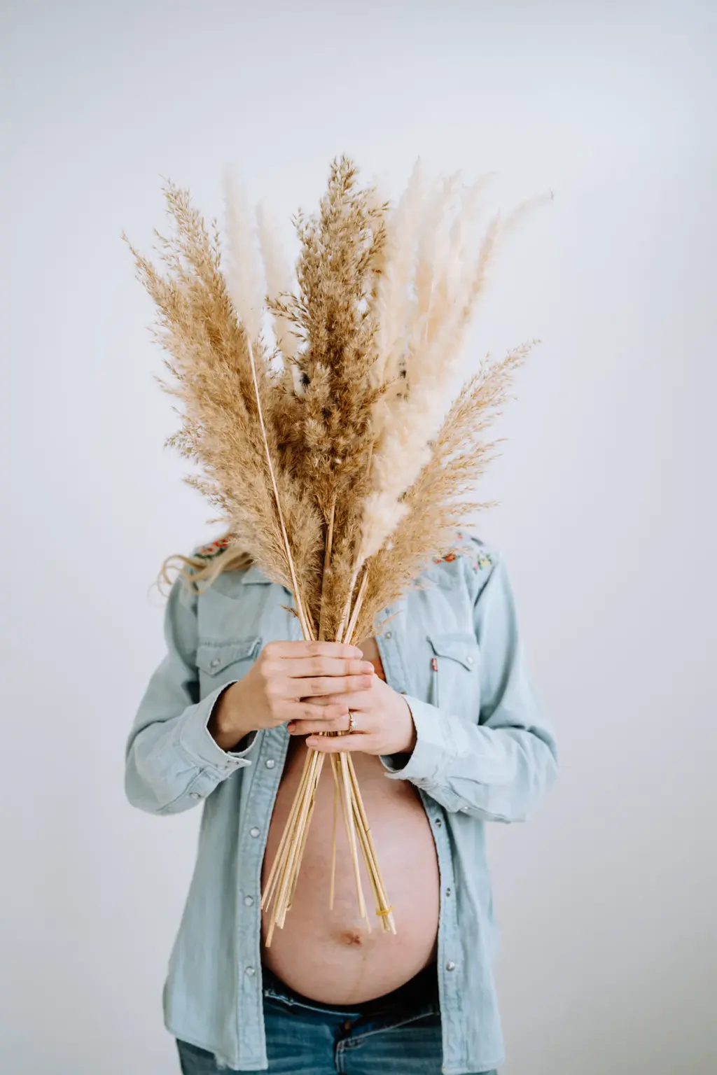 Ungewöhnliche Babybauchfotos mit Trockenblumen vor einem weißen Hintergrund