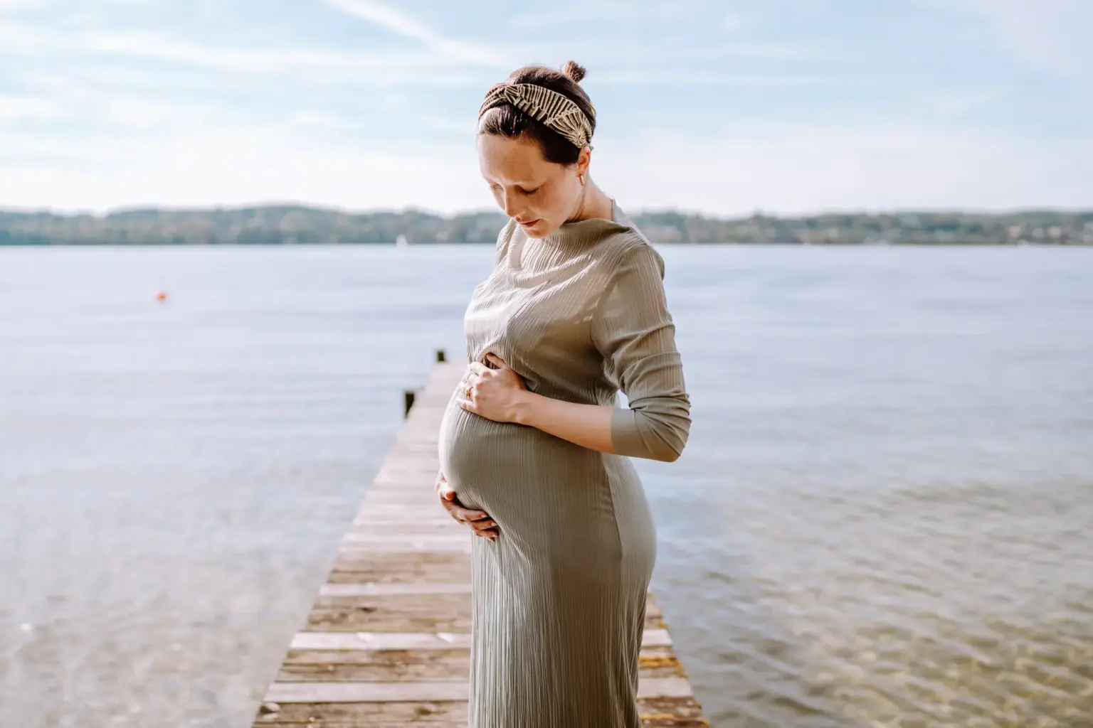 Frau steht auf dem Steg in Tutzing am Starnberger See und hält ihren Babybauch