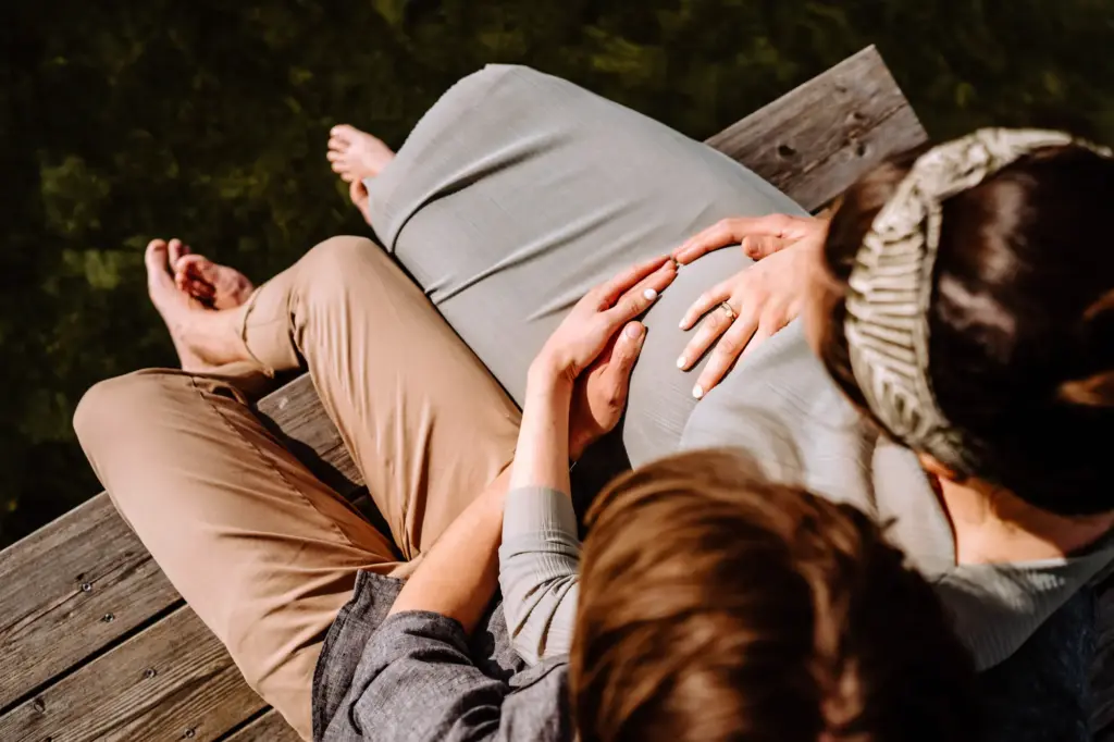 Paar sitzt auf dem Steg, Füße nah am Wasser, Babybauchfoto