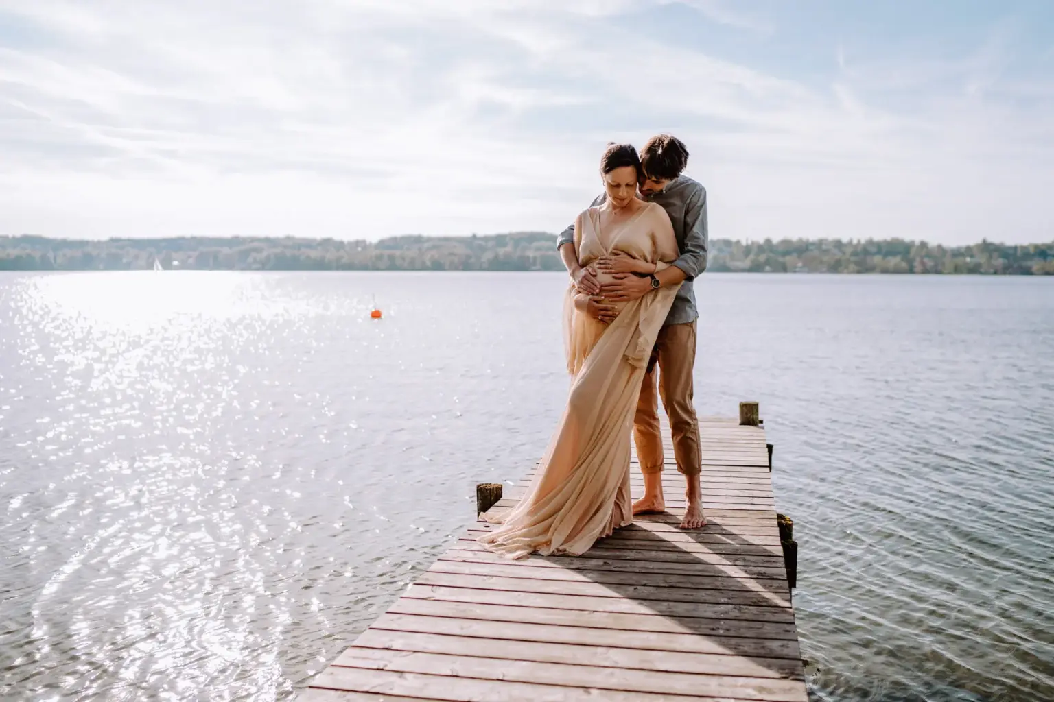 Schwangere hält Kleid und Bauch, Steg und Wasser im Hintergrund
