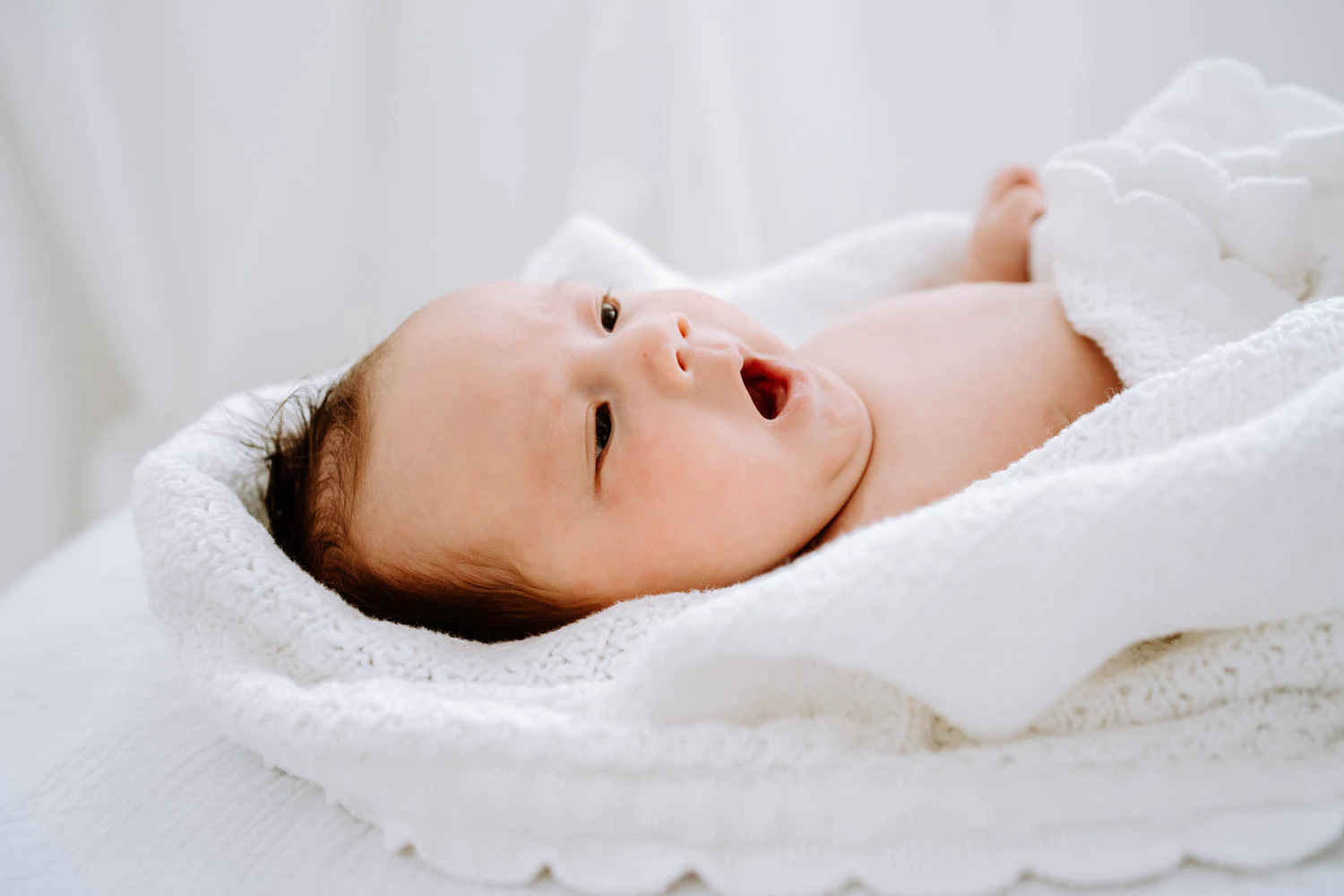 Baby gähnt entspannt, eingewickelt in eine weiße Decke