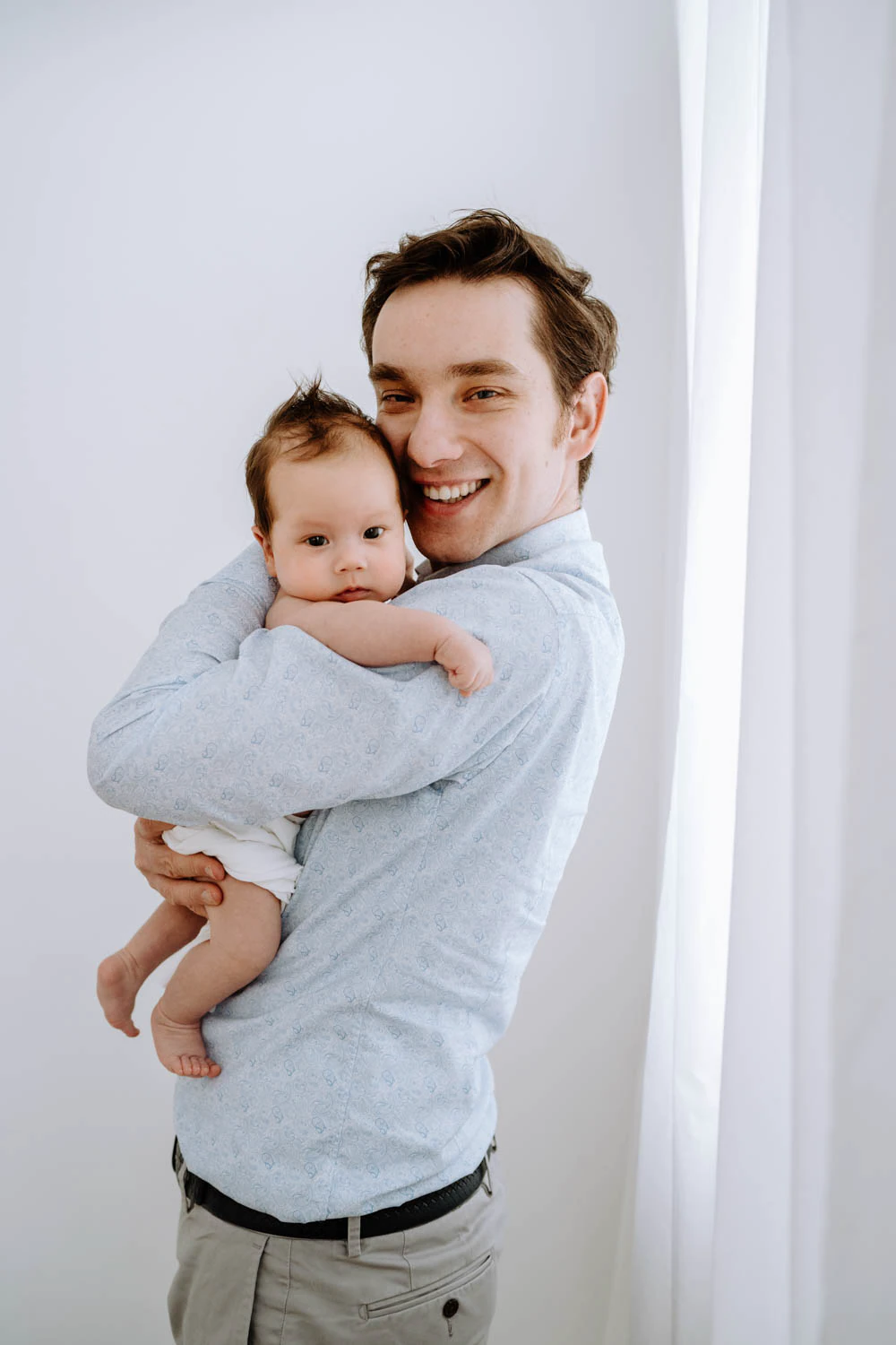 Papa hält Baby nah am Herzen, cleanes Studio Setting, viel Weiß