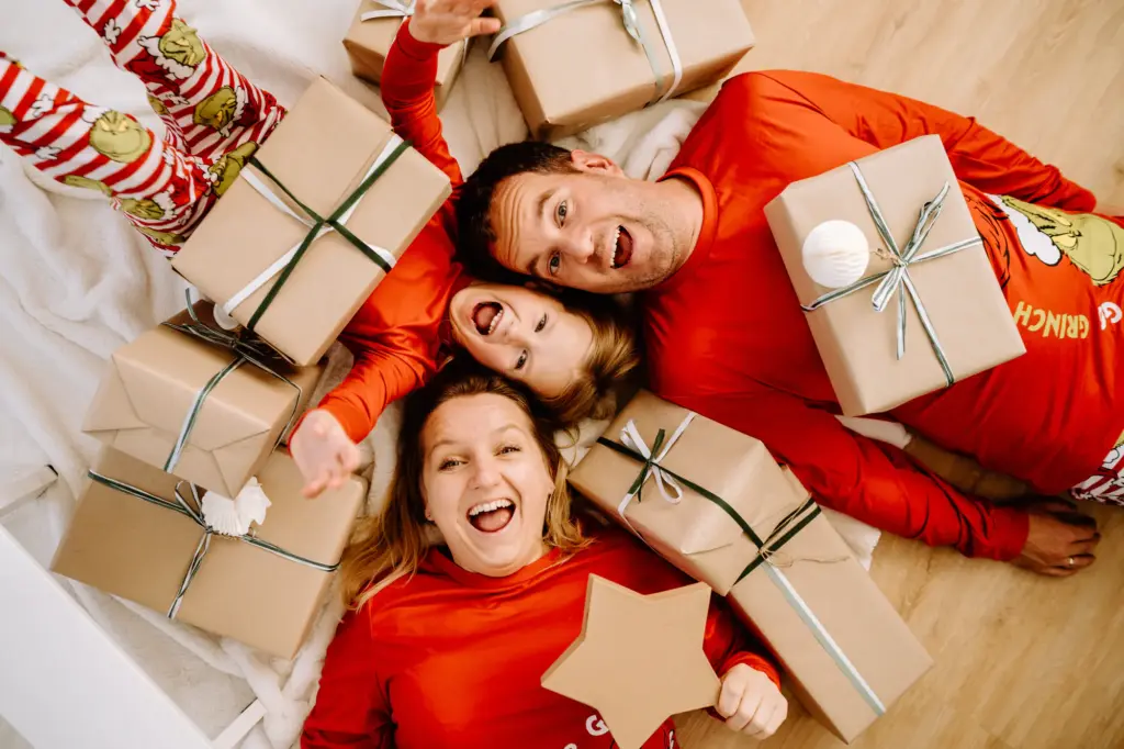 Drei lachende Erwachsene liegen zwischen weihnachtlich verpackten Geschenken