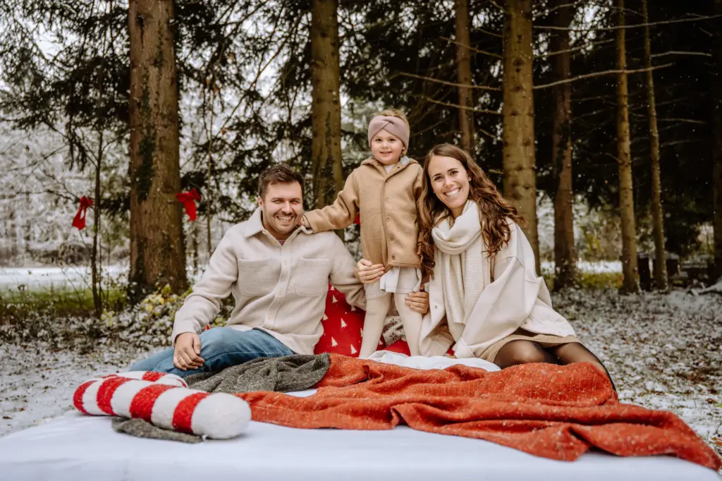 Lachende Familie sitzt mit ihrem Kind auf Decken im verschneiten Wald