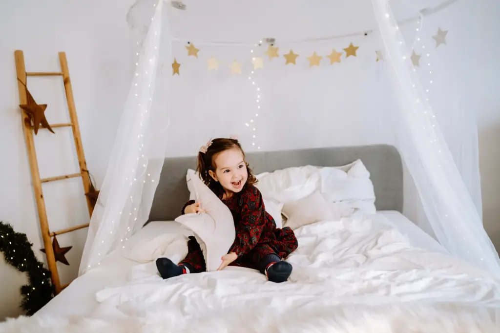 Lachendes Mädchen sitzt in einem festlich beleuchteten Weihnachtszimmer auf dem Bett