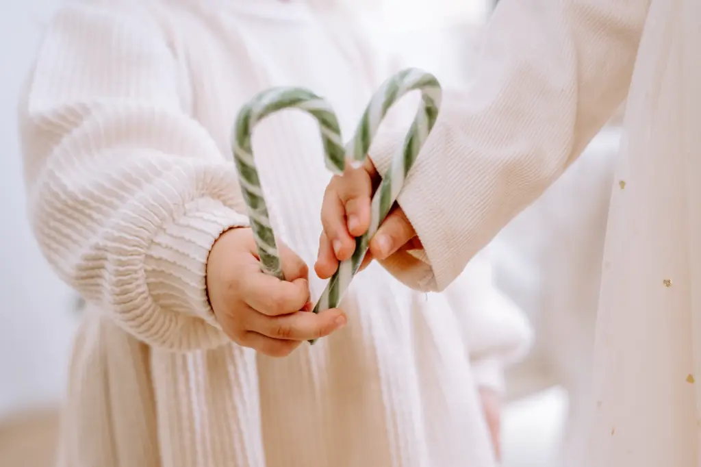 Zwei Kinderhände formen mit grün-weißen Zuckerstangen ein Herz
